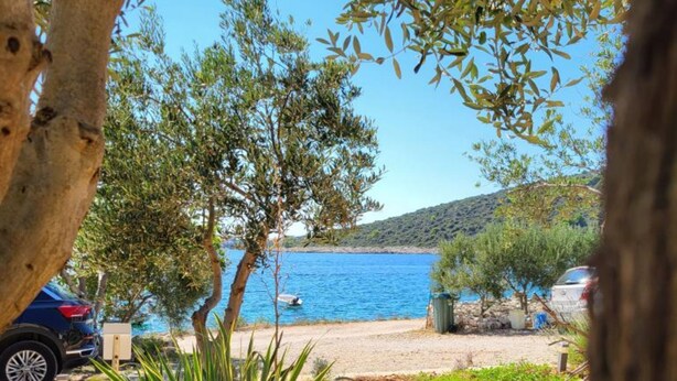 A coastal view with a parked car, a small boat, and a clear blue sea. - Apartments Radacic (Marina)