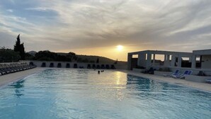 Una piscina con sillones de descanso y un cielo iluminado por el sol.