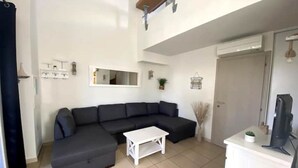 Una sala de estar con un sofá modular gris oscuro, una mesa de centro blanca, un televisor de pantalla plana sobre un mueble blanco y un espejo grande en la pared.