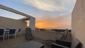 Terraza en la azotea con vistas al atardecer, mobiliario exterior e iluminación con luces colgantes.
