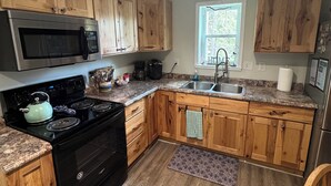 A kitchen with wooden cabinets, a black stove, a microwave, and a sink.