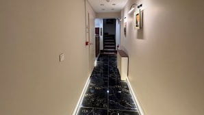 Un pasillo con suelo de mármol negro, paredes blancas y una escalera que sube a otro nivel.