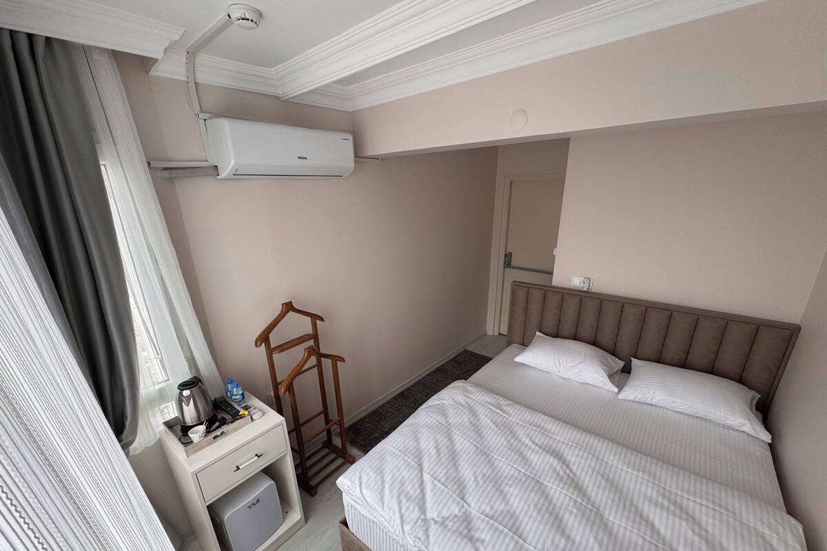 Hotellihuone, jossa on sänky, yöpöytä ja seinälle asennettu ilmastointilaite.