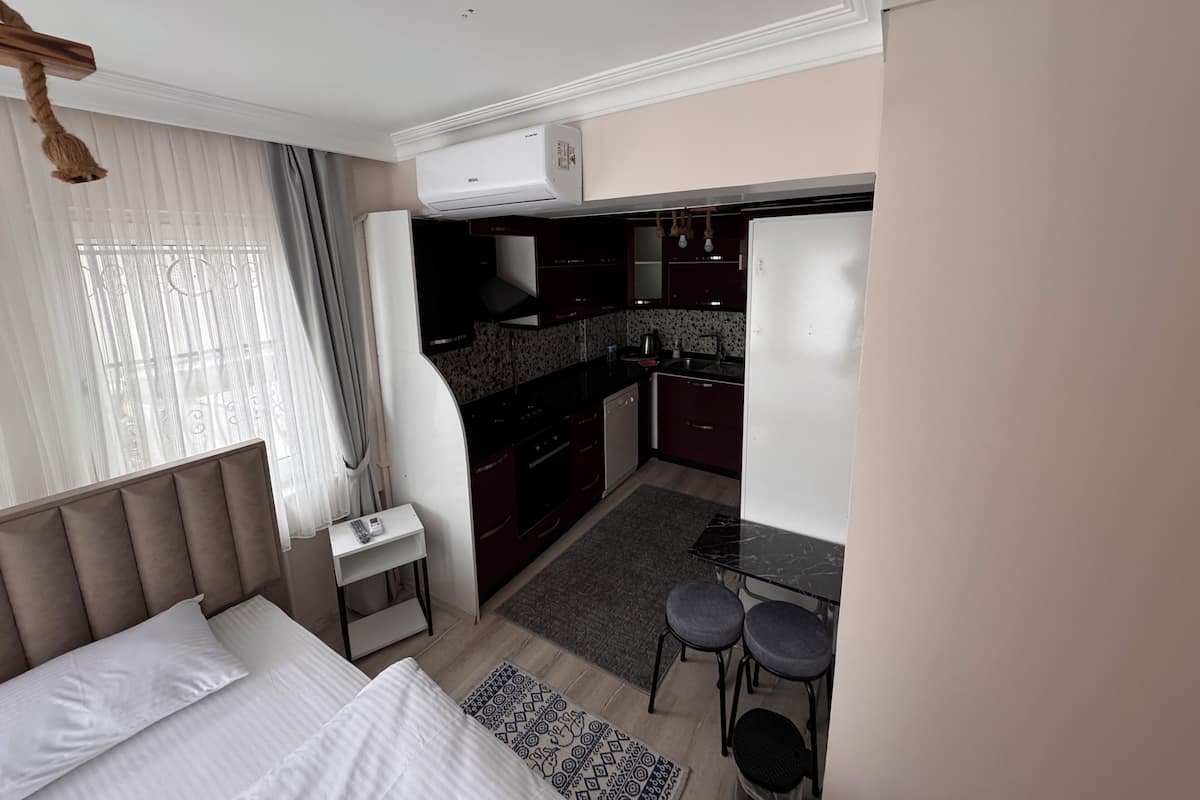 Pieni hotellihuone, jossa on sänky, yöpöytä ja pieni keittokomero.