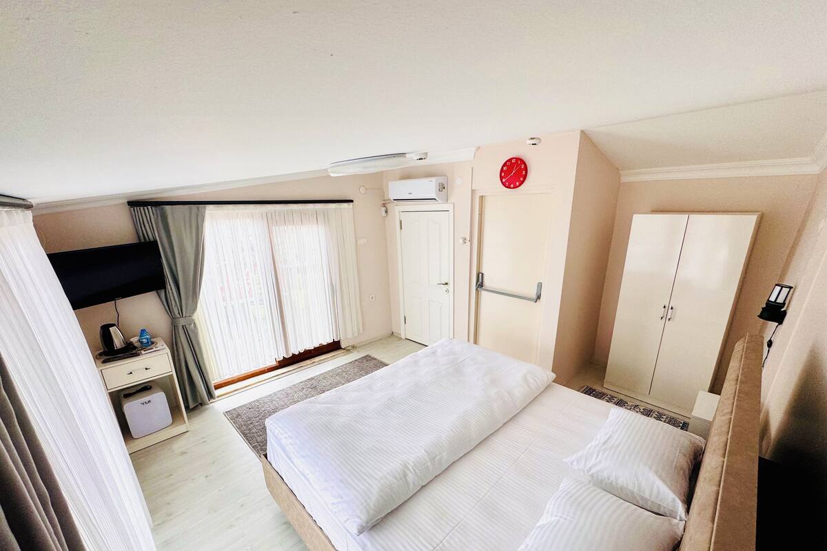 Hotellihuone, jossa on sänky, vaatekaappi, työpöytä ja ikkuna, jossa on verhot.