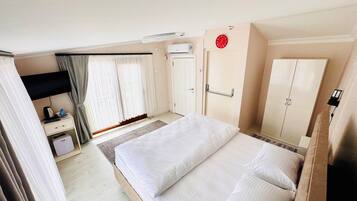 A hotel room with a bed, a wardrobe, a desk, and a window with curtains.
