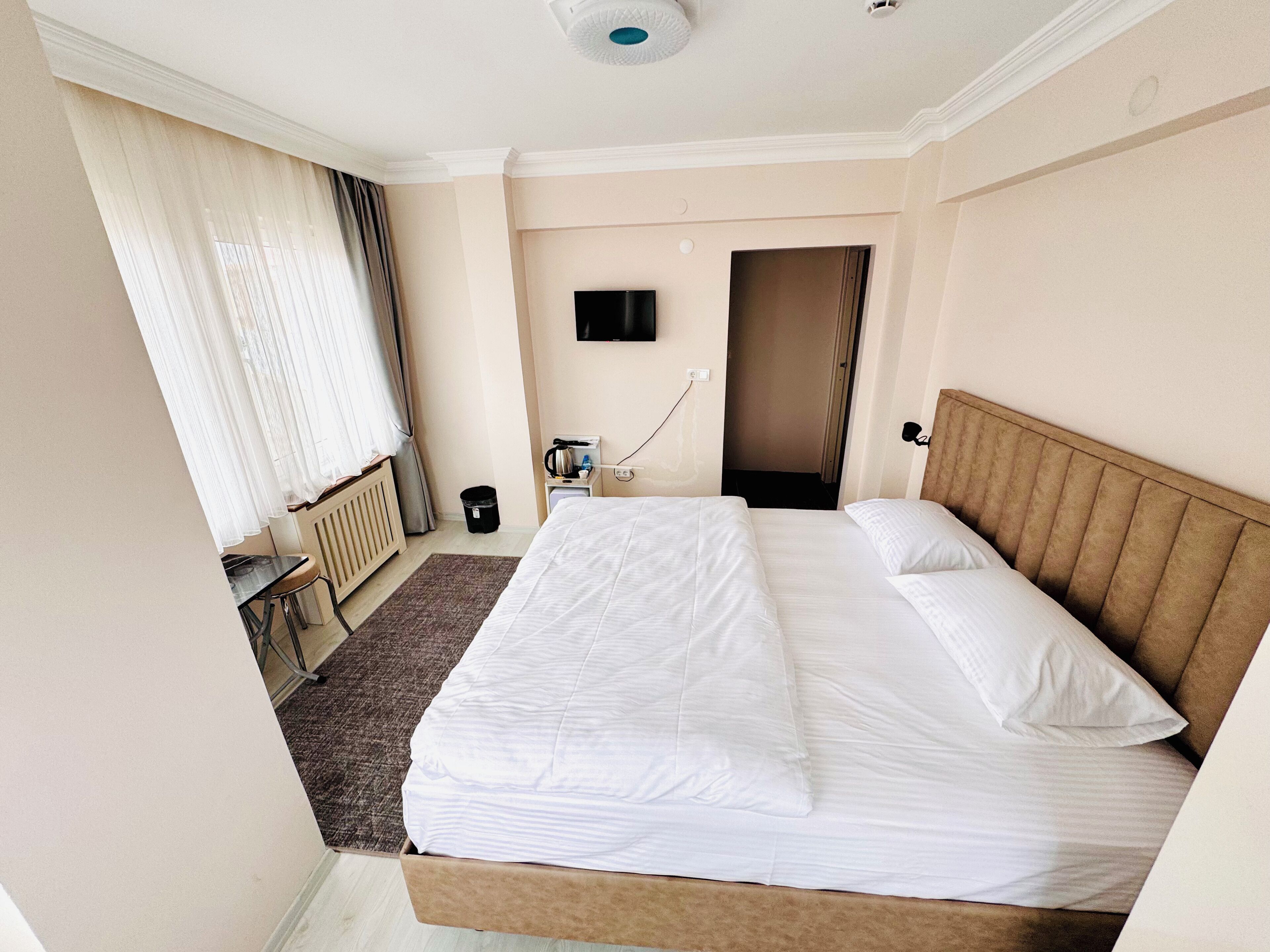 A hotel room with a large bed, a desk, a chair, a TV, and a door leading to another room.