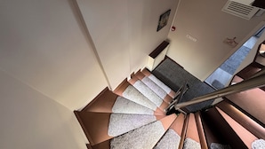 Una escalera de caracol con barandilla, peldaños alfombrados y un respiradero en la pared.