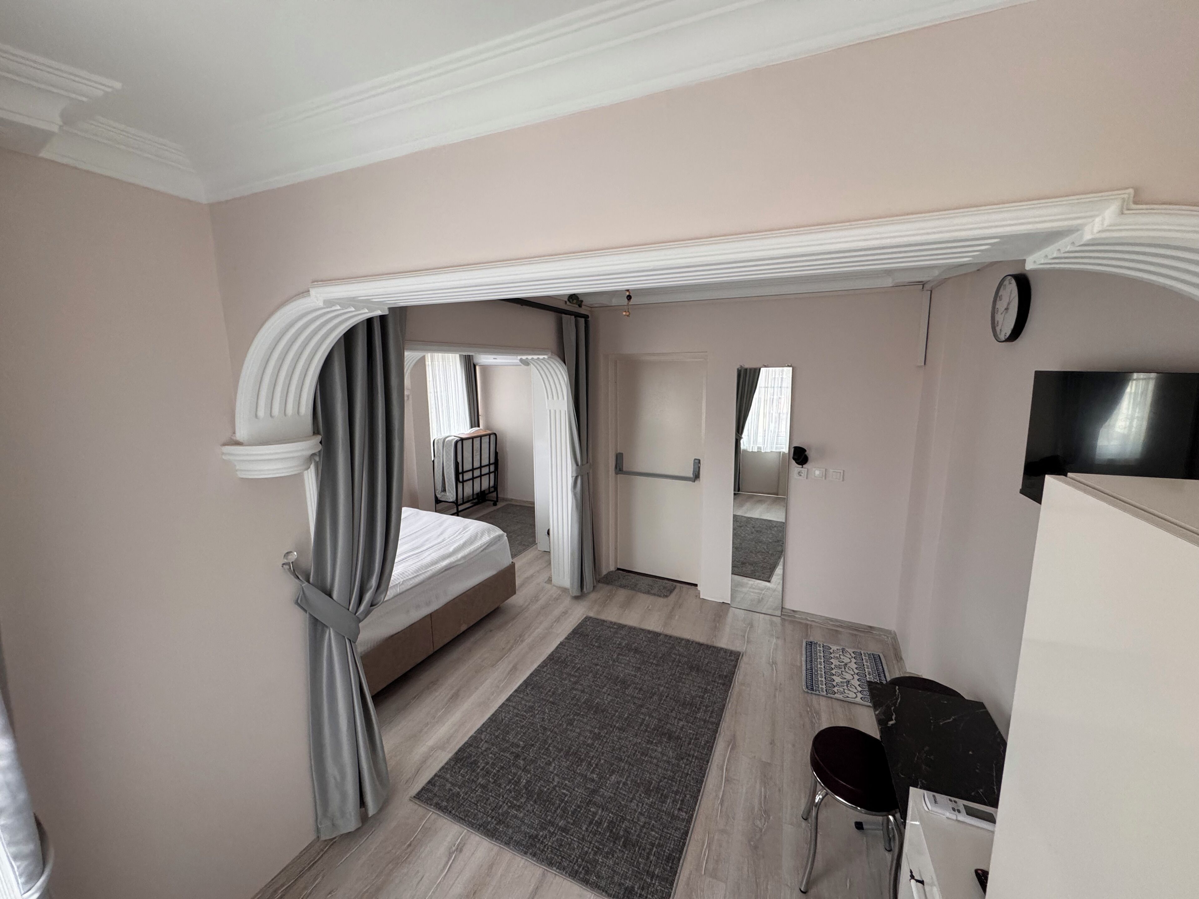 A bedroom with a bed, a desk, a chair, a TV, and a bathroom visible through an archway.