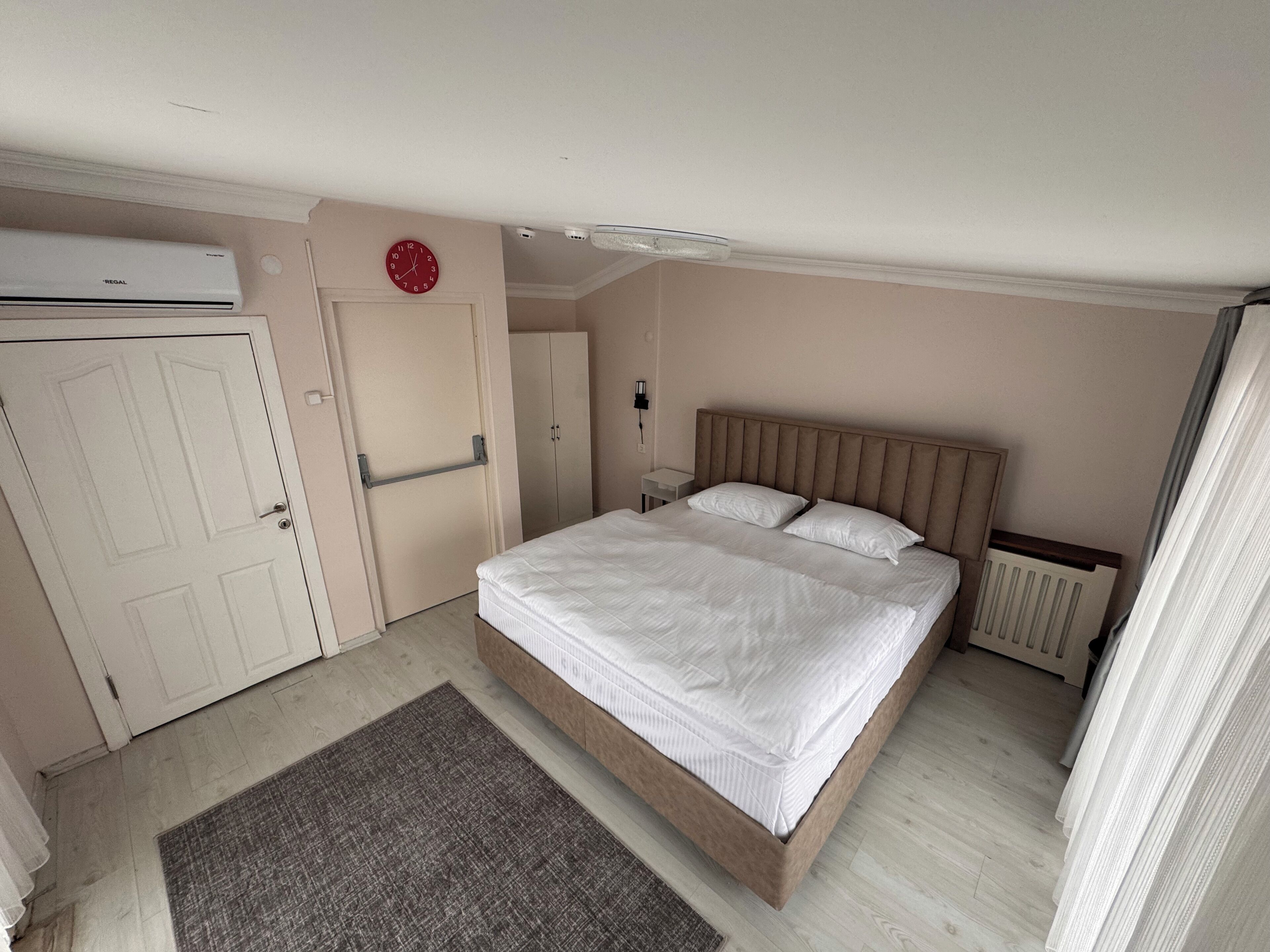 A bedroom with a bed, a radiator, a door, and a clock on the wall.