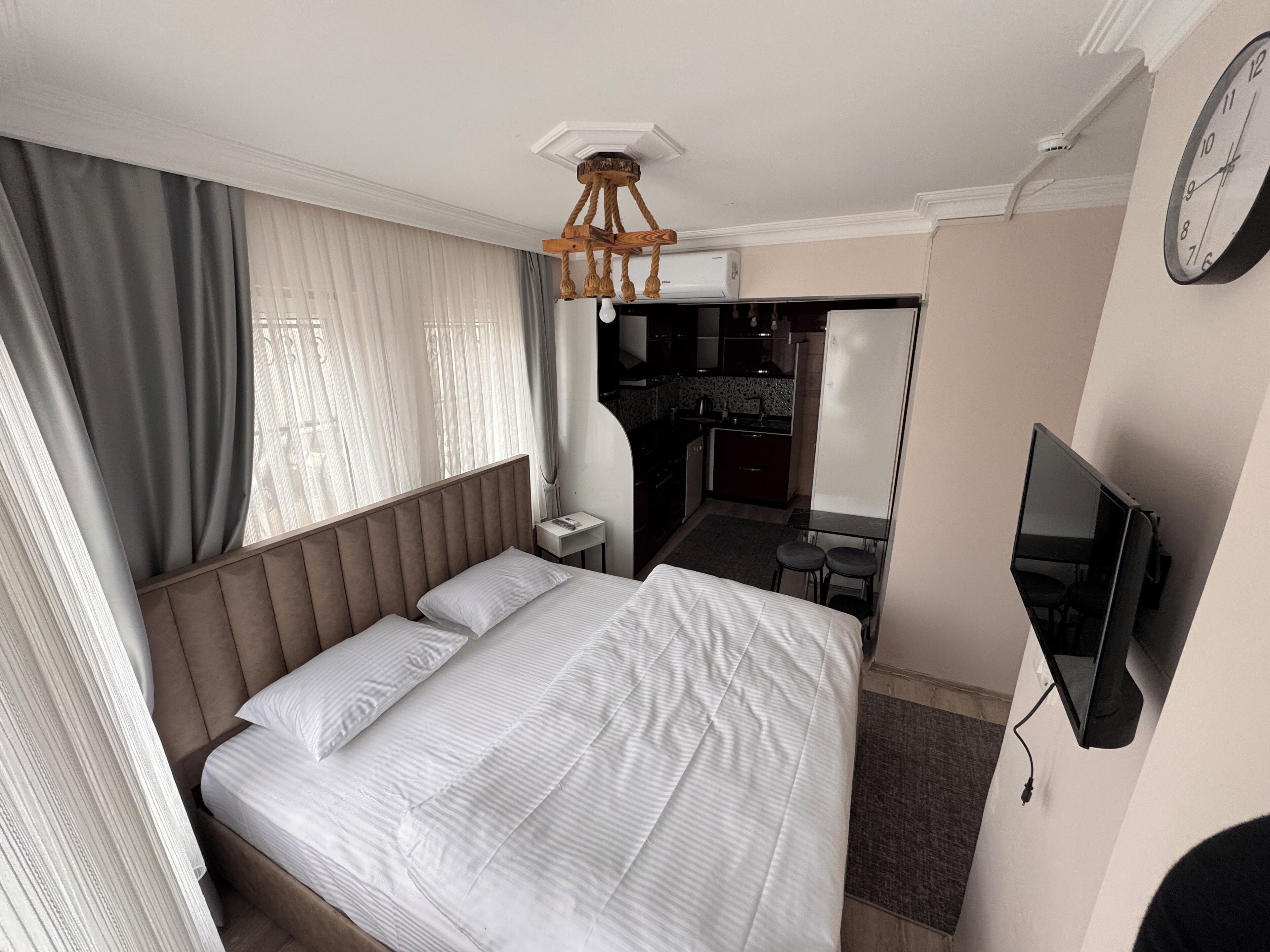 Habitación de hotel con una cama grande, televisor, una kitchenette pequeña y un baño visible a través de una puerta abierta.