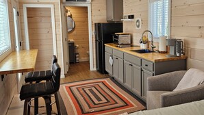 Een compacte keuken met houten wanden, een eethoek met tafel en stoelen, een kitchenette met koelkast en fornuis, en een raam met luxaflex.