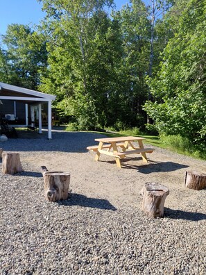 A gravel area with a wooden picnic table and three tree stumps. - Peaceful Getaway: Tiny Home Studio in Sedgwick, Maine (Sedgwick)