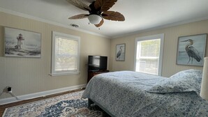 Een slaapkamer met een bed, een plafondventilator, een televisie en kunstwerken aan de muren.