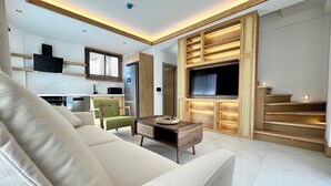 Ein modernes Wohnzimmer mit einer Couch, einem Couchtisch, einem Fernseher und einer Küchenzeile im Hintergrund.