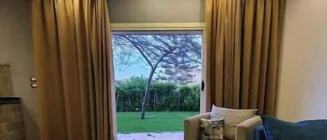 Ein modernes Wohnzimmer mit einer Couch, einem Holztisch und Blick auf einen Garten durch eine Glastür.