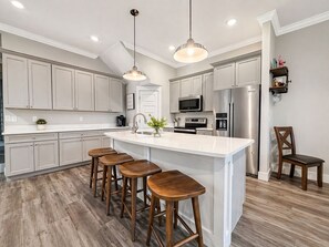 A modern kitchen with a central island, bar stools, stainless steel appliances, and pendant lighting. - One block to beach! Spacious group getaway with Rooftop Deck & Game Room! (Panama City Beach)