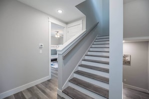A staircase with wooden steps leading to a landing, a white wall, and a ceiling fan in the background.