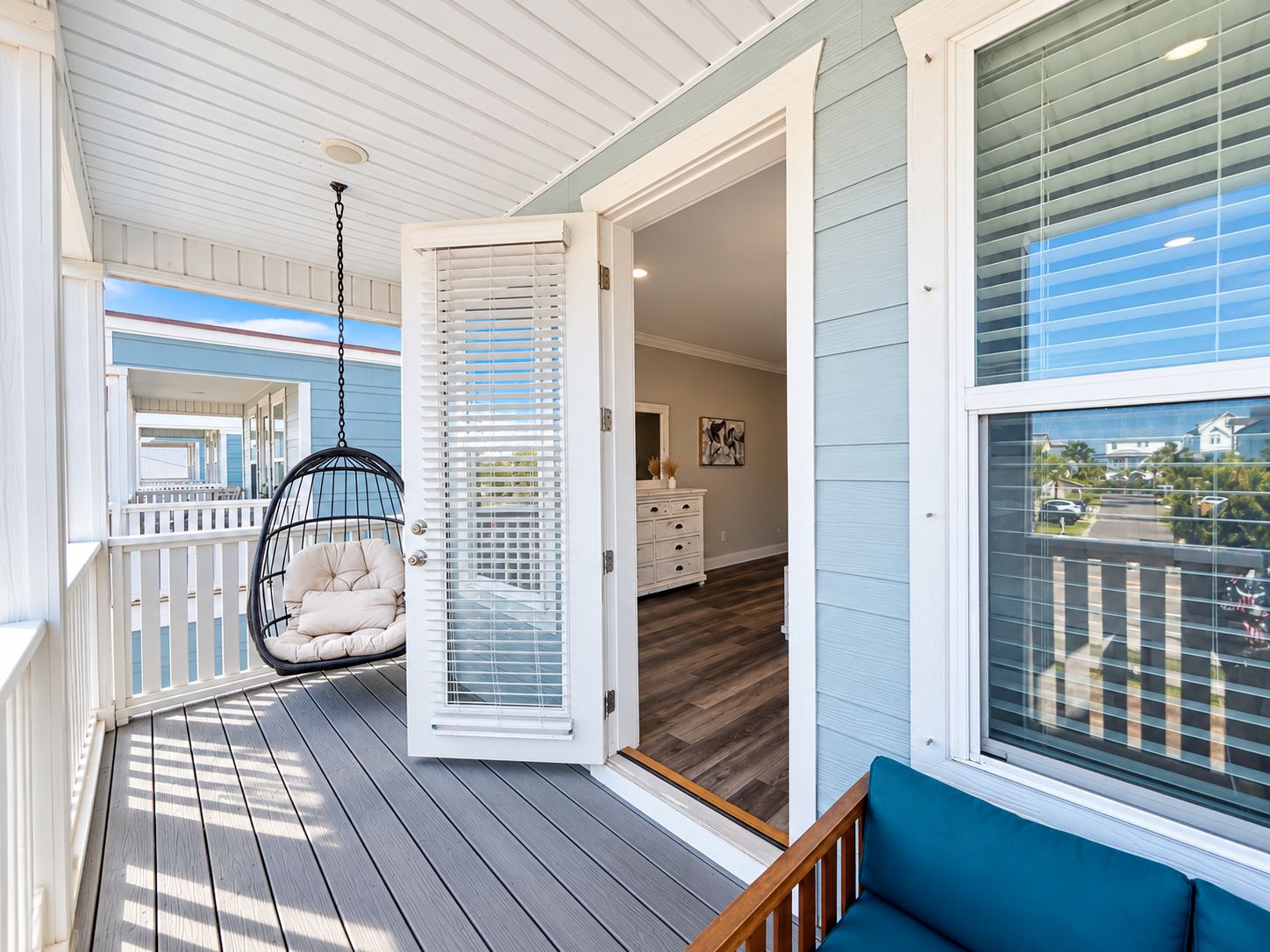 A covered porch with a hanging chair, a wooden deck, and a view of the interior through an open door.