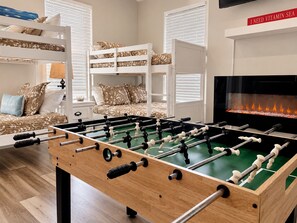 A room with a foosball table, bunk beds, a fireplace, and a television.