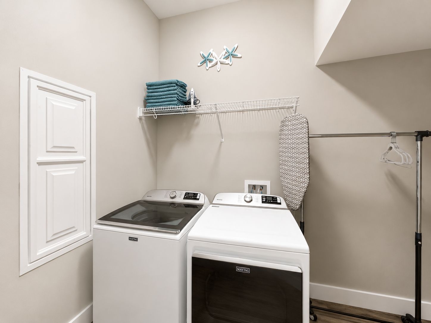 A laundry room with two Maytag washing machines, a drying rack, and a hanging iron.