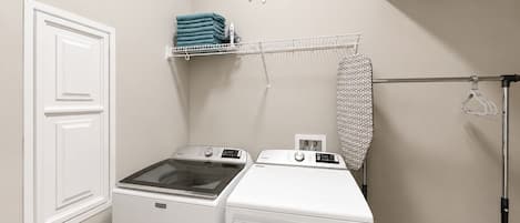 A laundry room with two Maytag washing machines, a drying rack, and a hanging iron.