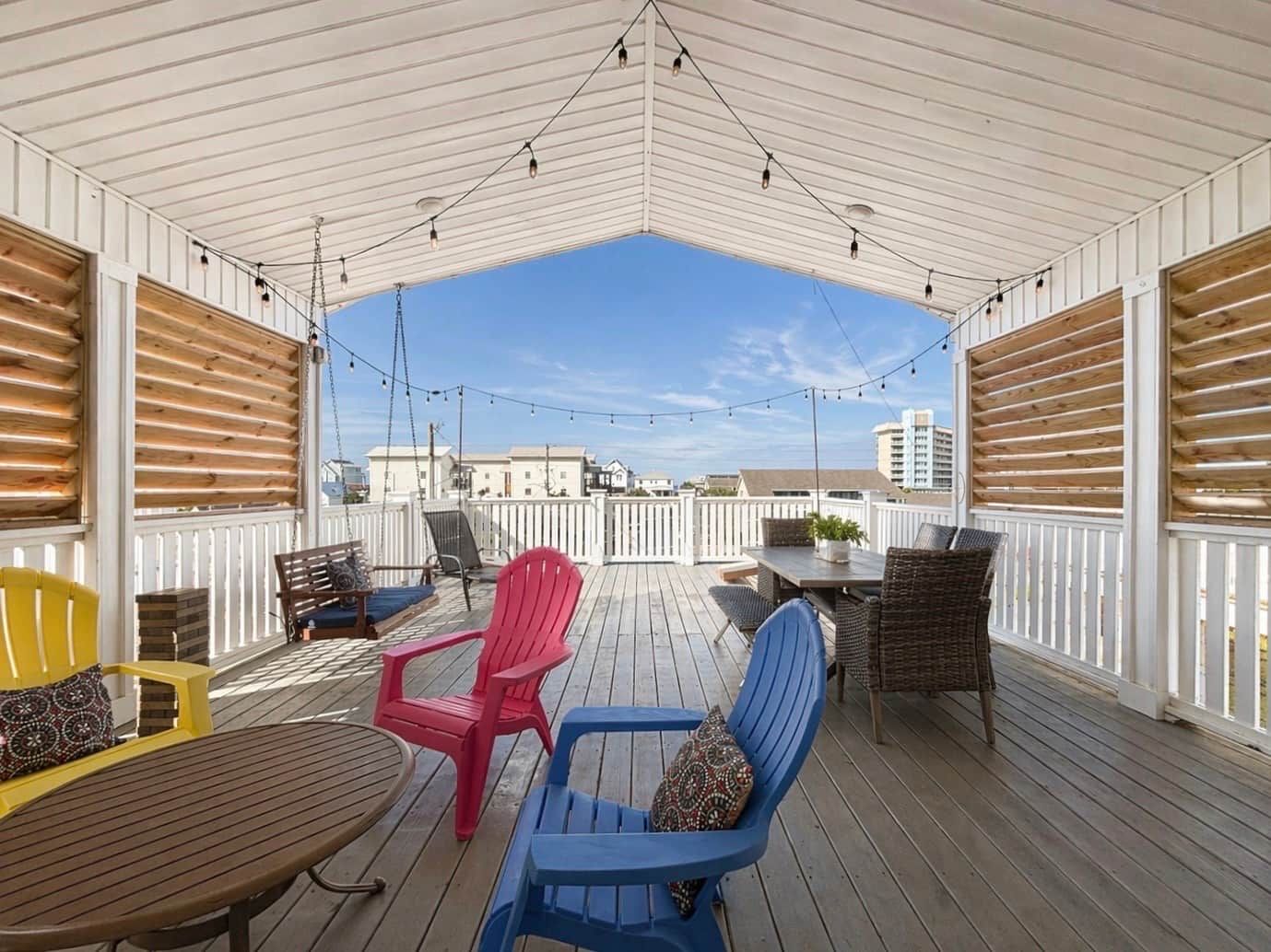 An outdoor deck with a covered area, furnished with chairs and tables, and string lights overhead.