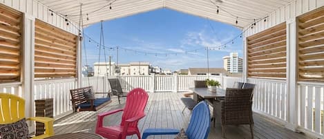 An outdoor deck with a covered area, furnished with chairs and tables, and string lights overhead.