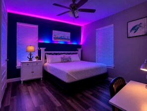 Un dormitorio con cama, mesitas de noche, ventilador de techo y escritorio.
