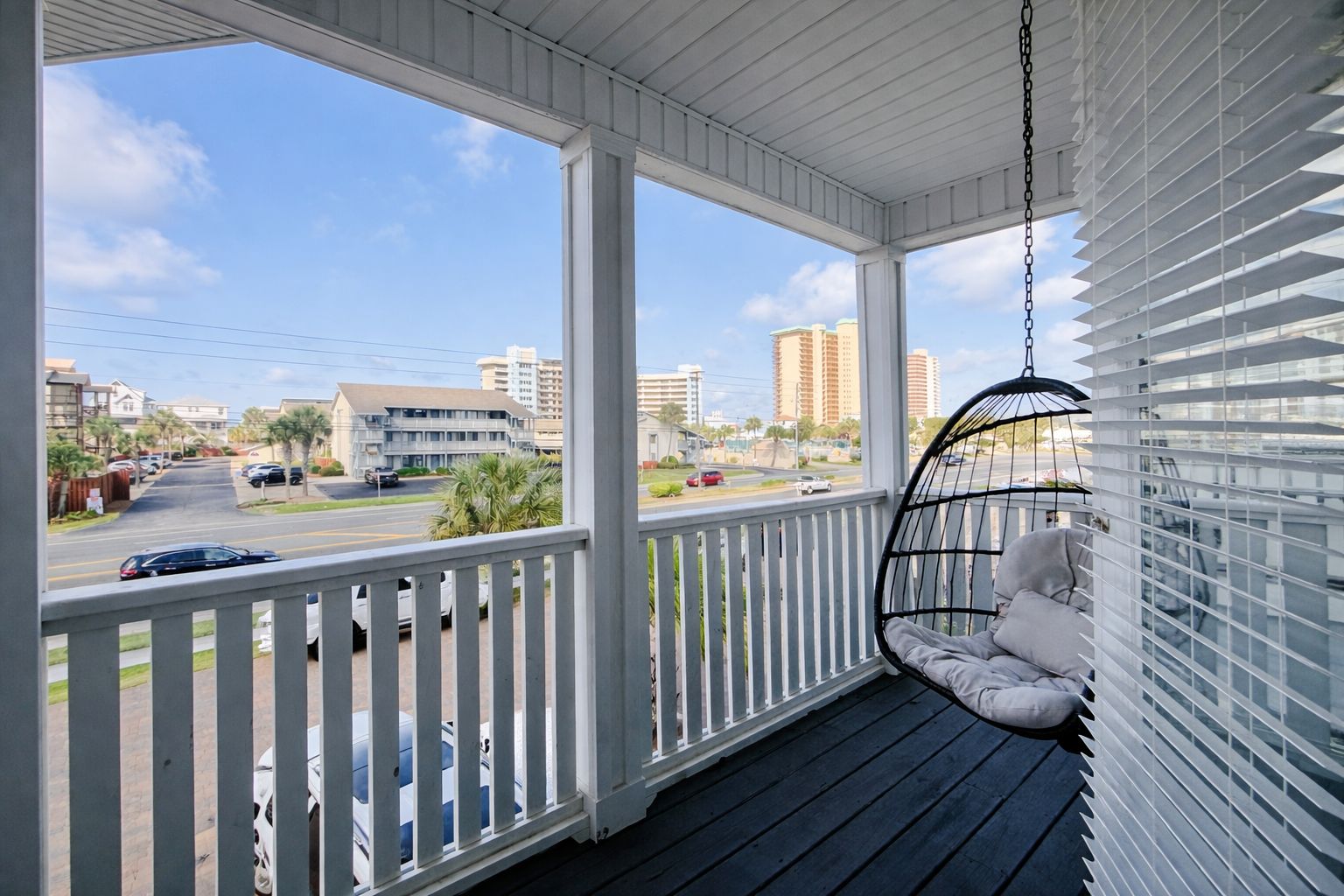 A porch with a hanging chair, a view of a street with cars, and buildings in the background.