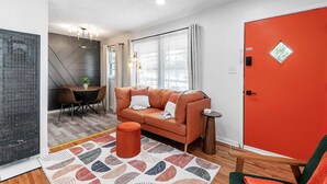 A modern living room with a sofa, a dining table, and a red door.