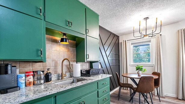 A modern kitchen with green cabinets, a granite countertop, and a dining area with a table and chairs.