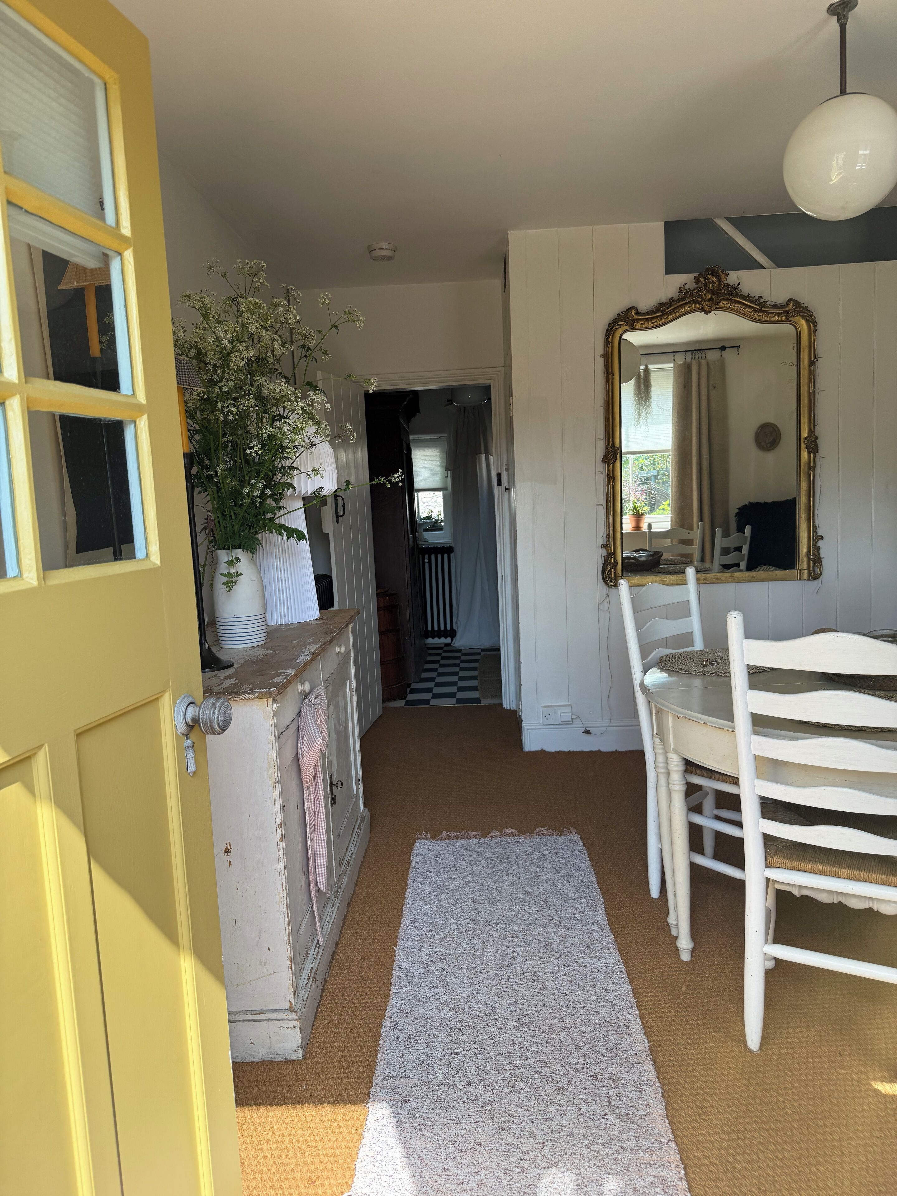 A hallway with a yellow door, a white dresser, a mirror, and a checkered floor.