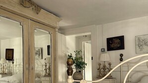 Een slaapkamer met een grote spiegel, een bed met een wit hoofdeinde, een dressoir en een nachtkastje met een lamp.