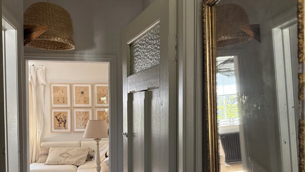 Een gang met een witte deur die leidt naar een woonkamer met een bank en een lamp.