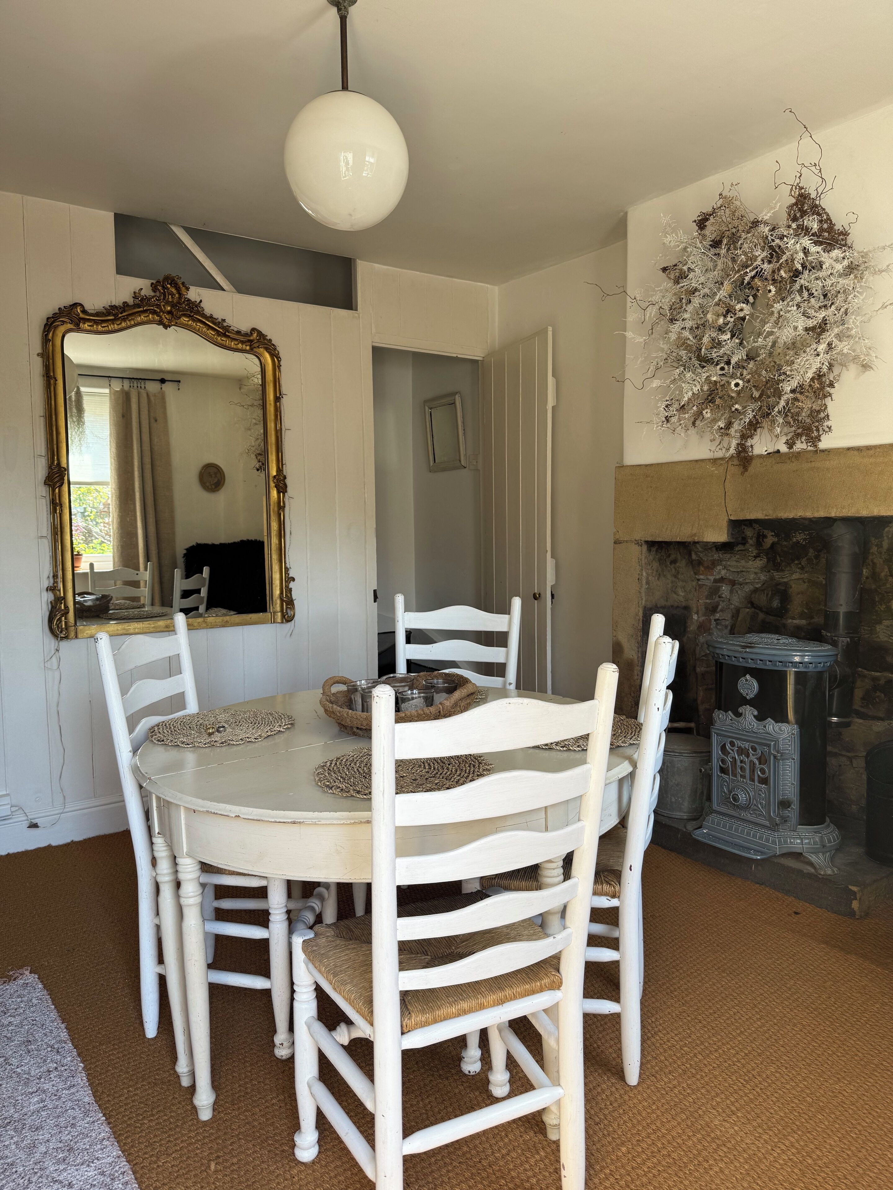 A dining area with a round table, white chairs, a large mirror, and a decorative wall piece.