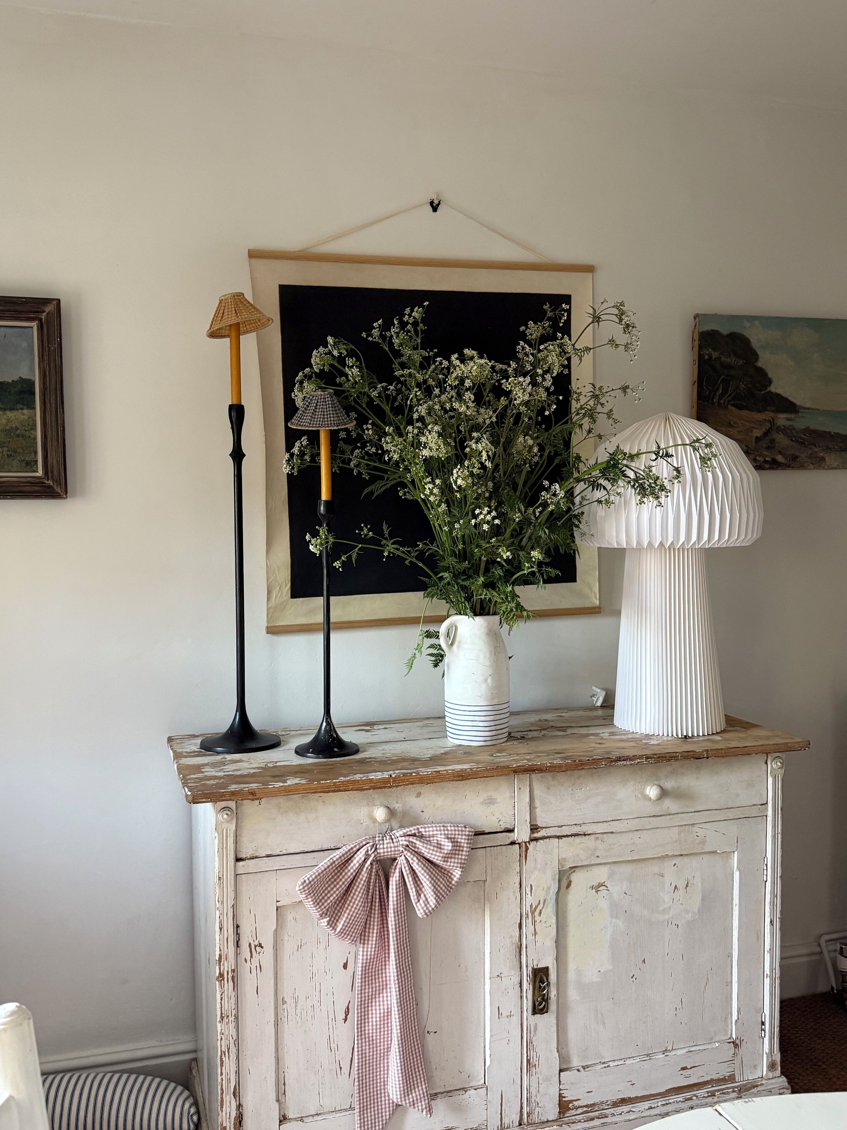 A rustic wooden dresser with a white vase of flowers, a black lamp, and a white lamp with a pleated shade.