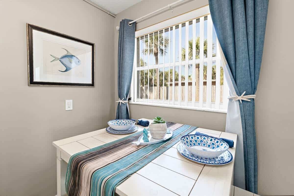 A dining area with a table set for two, featuring blue and white patterned plates, a striped table runner, and a framed fish artwork on the wall.