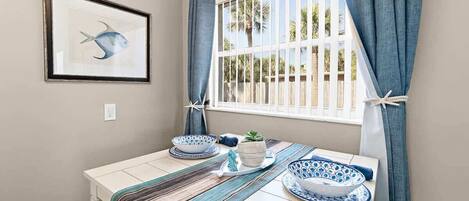 A dining area with a table set for two, featuring blue and white patterned plates, a striped table runner, and a framed fish artwork on the wall.