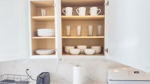 Una cocina con un armario empotrado que contiene vajilla y tazas blancas, un tostador y una estufa a gas.