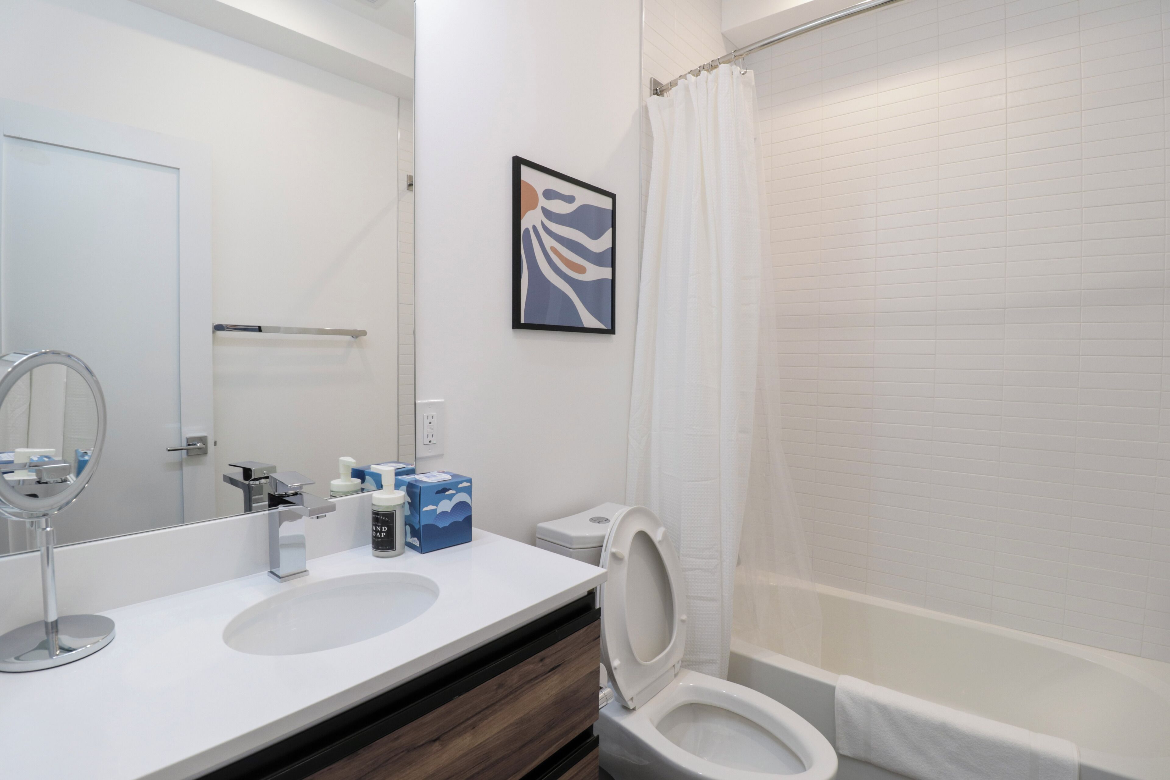 Une salle de bain moderne avec un lavabo blanc, un miroir, des toilettes et un rideau de douche.