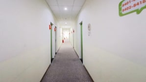 Een lange, smalle gang met groene deuren aan beide zijden en een vloerbedekking.