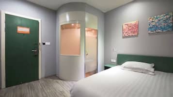 A hotel room with a bed, a green door, a curved mirror, and two abstract paintings on the wall.