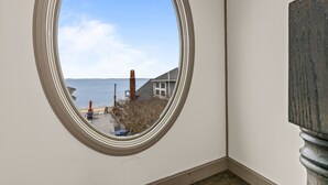 A room with a large oval window offering a view of a dock and a house by the water.