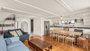 A modern living room with a sofa, a wooden coffee table, and a dining area with a long table and chairs.