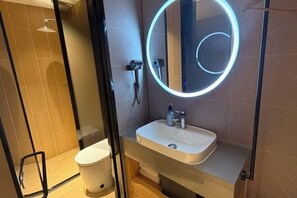 Een moderne badkamer met een douchecabine van glas, een witte wastafel en een spiegel met ronde verlichting.