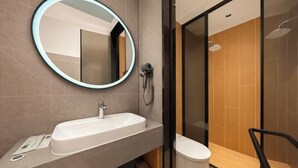 Une salle de bain moderne avec un miroir rond, un lavabo blanc, une douchette à main et des toilettes.