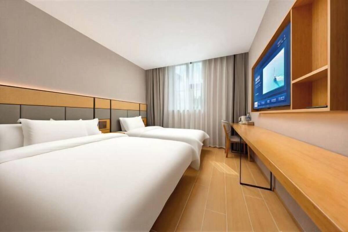Quarto de hotel moderno com duas camas, uma escrivaninha, televisão e uma janela grande com cortinas.