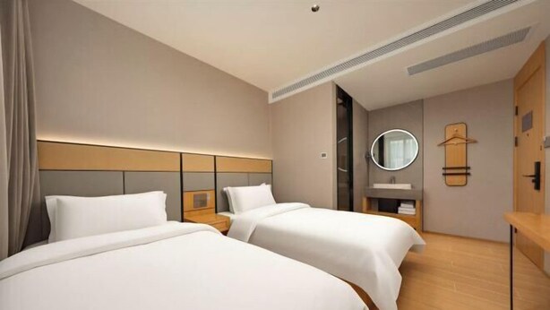Une chambre d’hôtel avec deux lits, une table de chevet, un miroir, un porte-manteau et un plancher en bois.