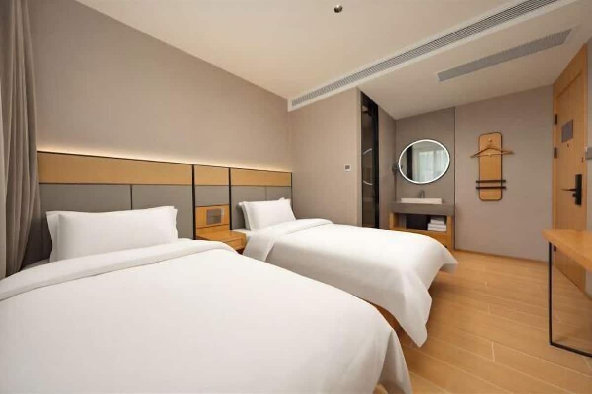 Quarto de hotel com duas camas, uma mesa de cabeceira, um espelho, um porta-roupas e piso de madeira.